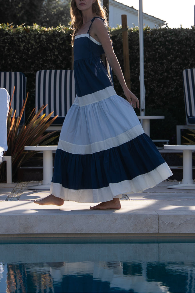 Woman walking along the edge of a pool, wearing a maxi dress with navy, ivory, and blue colour-block panels. 