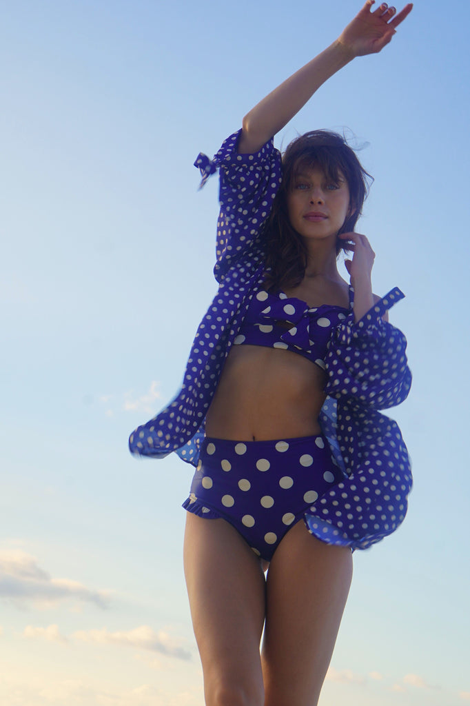 Woman in a blue polka dot bikini with a matching cover-up against a clear sky.