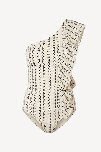 A one-shoulder ruffled swimsuit in cream with black dotted and wavy vertical line patterns, shown against a plain light gray background.