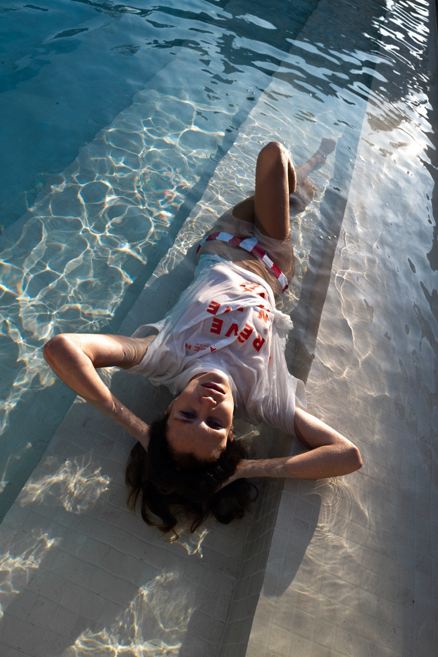 Woman wearing a graphic t-shrit and red and white stripe bikini pants lying in a pool