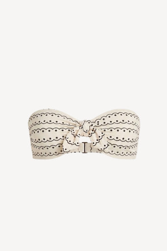 An off-white strapless bandeau top featuring a scalloped eyelet lace pattern and a central bow detail, set against a solid light gray background.