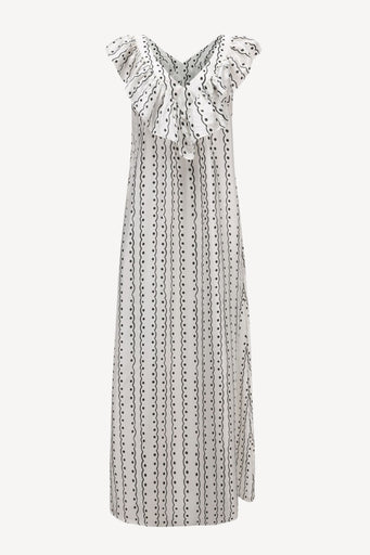 A sleeveless white dress with a black dotted vertical pattern and ruffled cap sleeves, featuring a tie-neck detail, shown against a plain light gray background.
