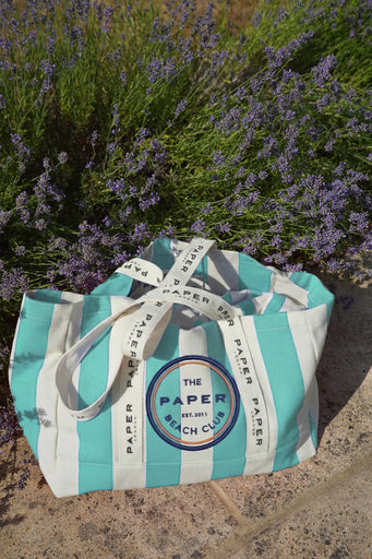 Striped tote bag with 'The Paper Beach Club' logo on a stone surface with lavender in the background
